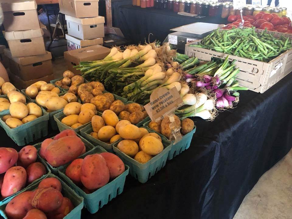 Fresh potatoes, onions, green beans, and tomatoes displayed at a farmers market.